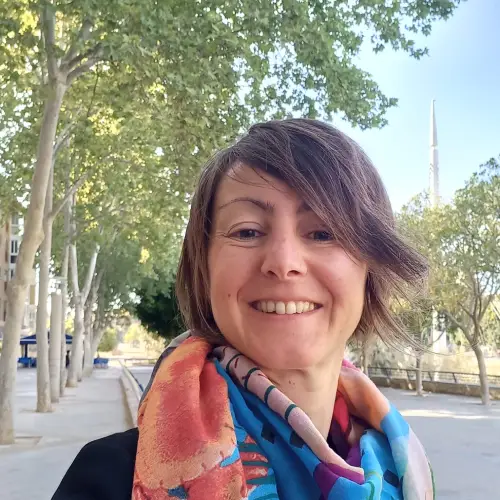 Mujer con pañuelo sonriendo delante delante de una ruta con árboles