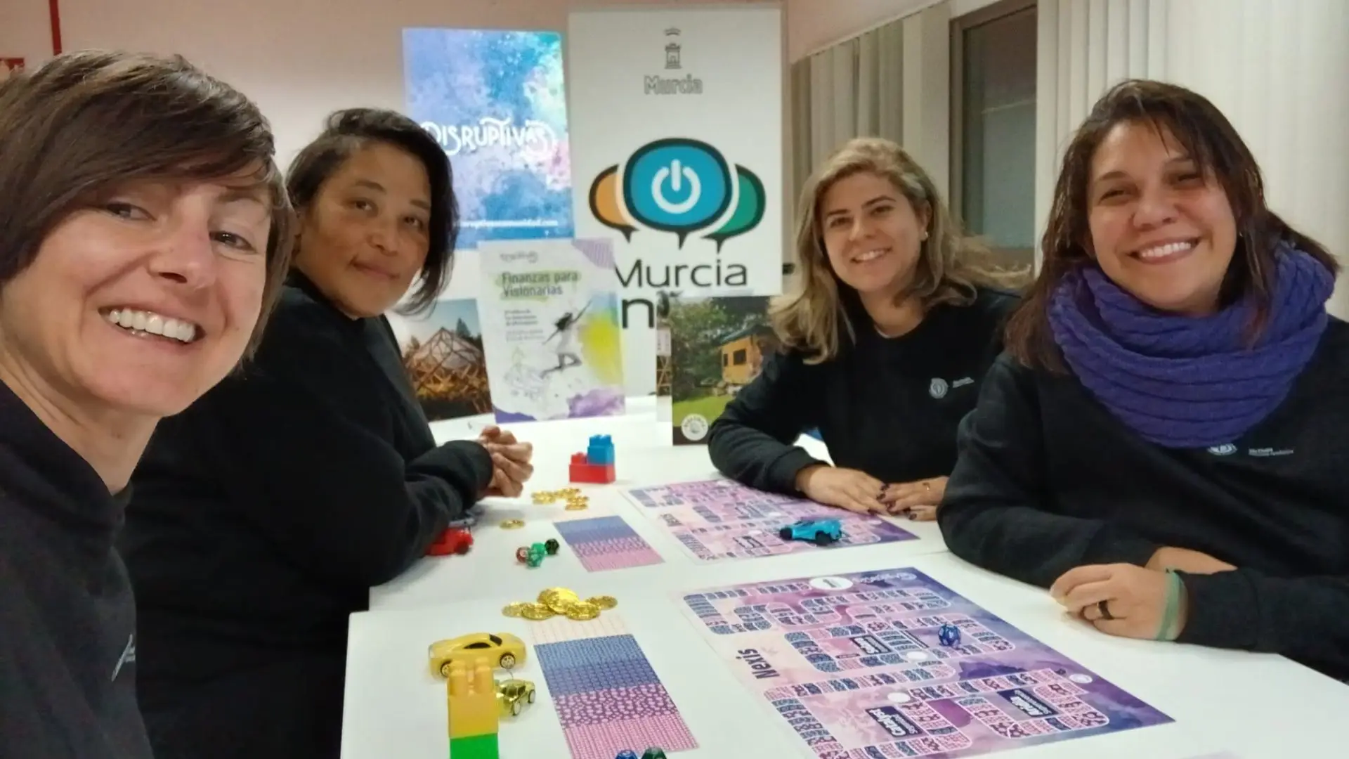 Mujeres sentadas sobre una mesa donde hay un tablero de juegos