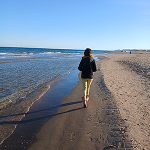 Mujer caminando en la orilla de la playa con el mar ba bañando la arena